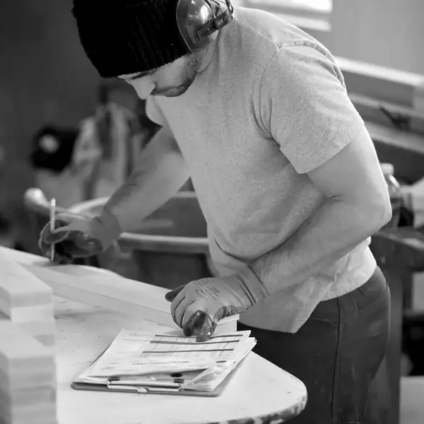 A craftsman in a knit cap and ear protection marks a stack of door parts