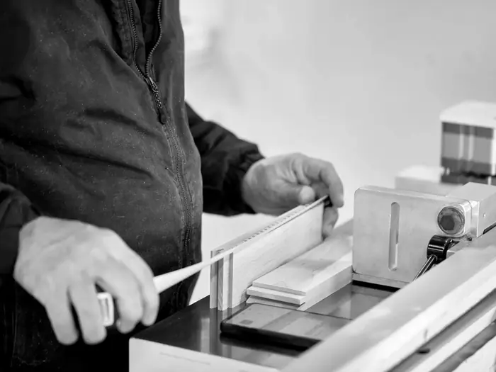 A craftsman checks a drawer side against the tape at the bench